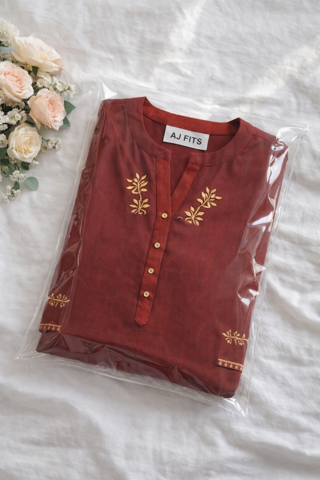 Folded red kurti with gold embroidery on a white surface with flowers